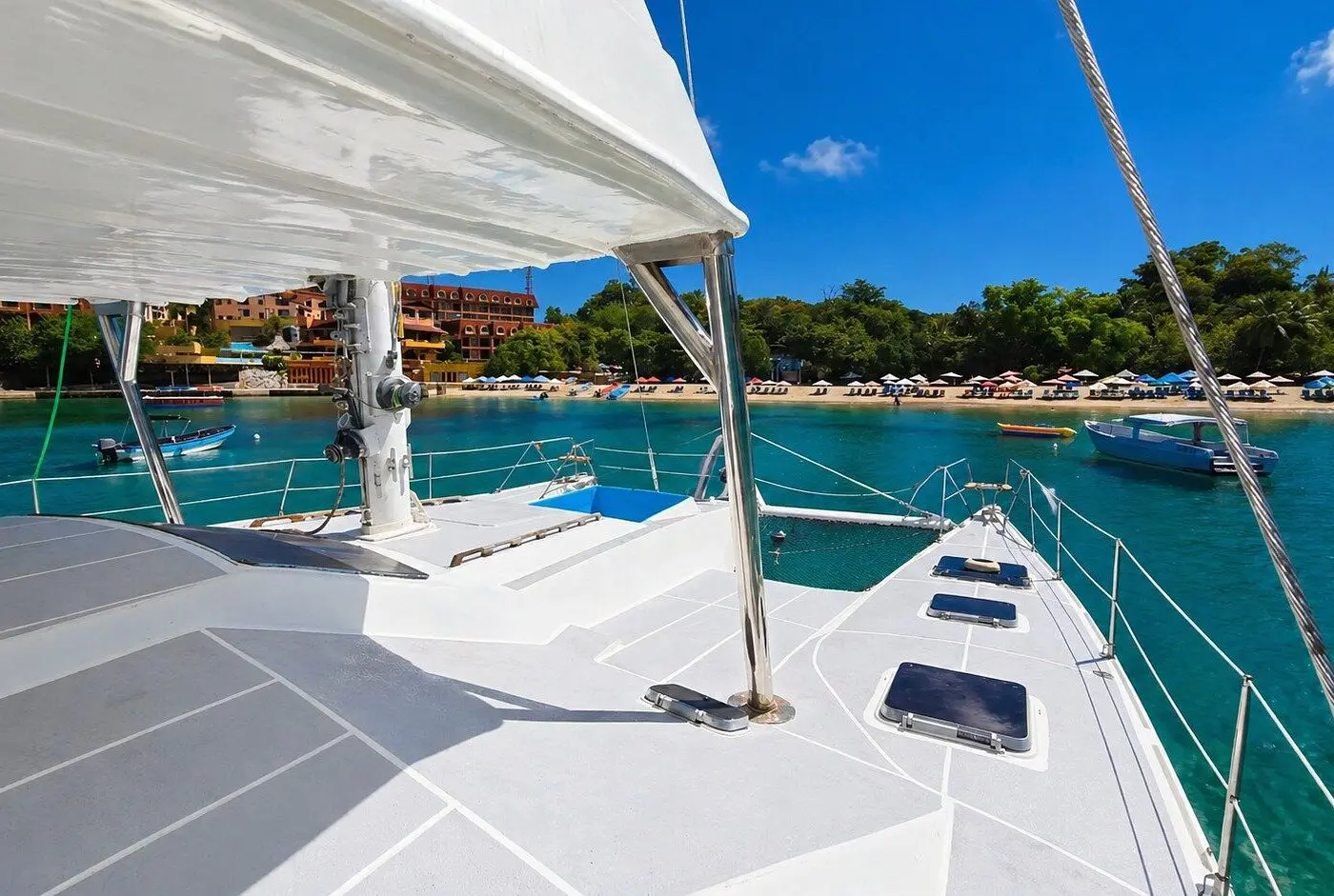 Deck of a sailing catamaran under the boom, anchored off a beach with umbrellas and resorts in Puerto Plata