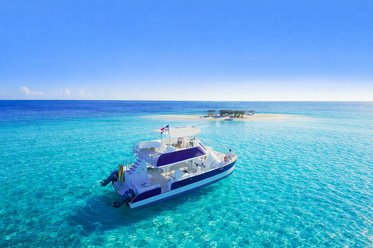 Power catamaran in clear turquoise shallows off the tiny sand cay of Cayo Arena
