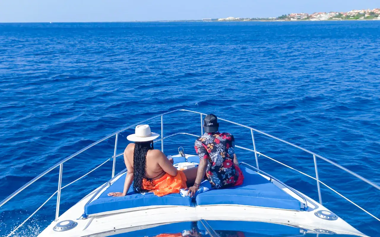 Two guests relaxing on the yacht's blue bow cushions, gazing over deep blue sea toward the Riviera Maya coast