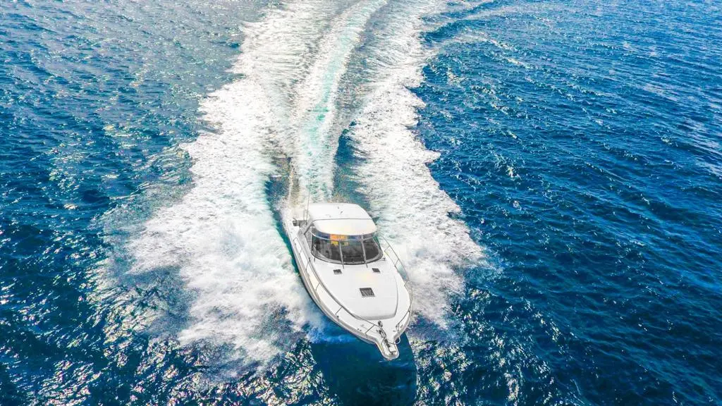 Aerial view of a motor yacht carving a curved white wake across deep blue water off Punta Cana