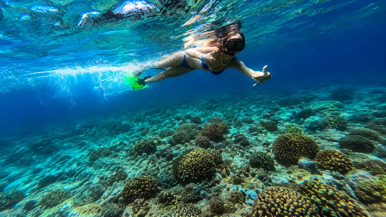A snorkeler in a mask and fins glides over coral heads in clear blue water