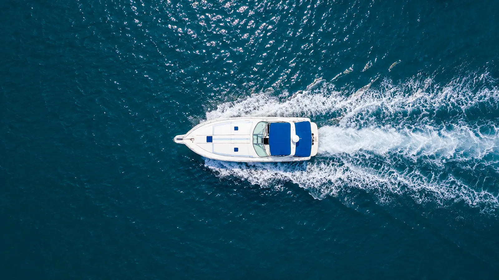 Overhead view of a white motor yacht leaving a long white wake on deep blue water