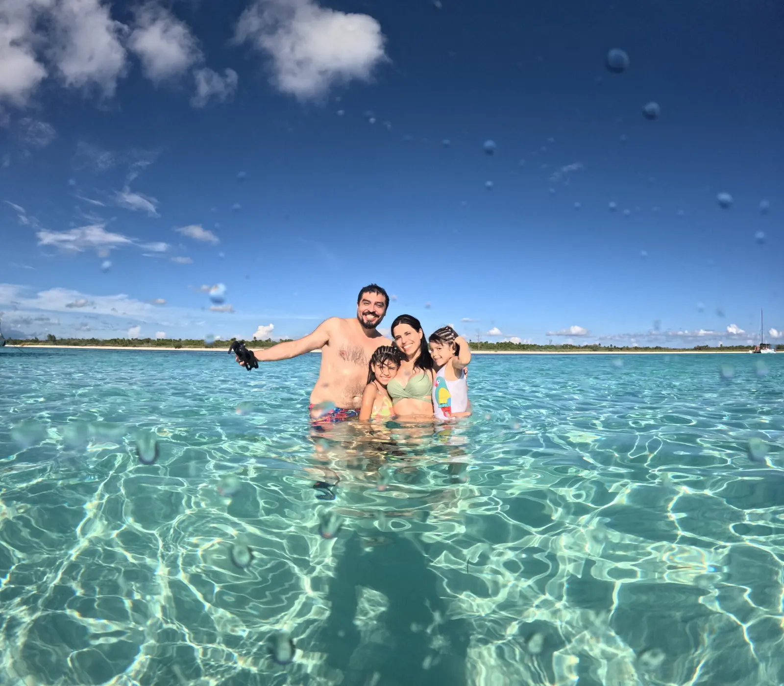 Family with two kids standing waist-deep in clear turquoise shallows off Cozumel