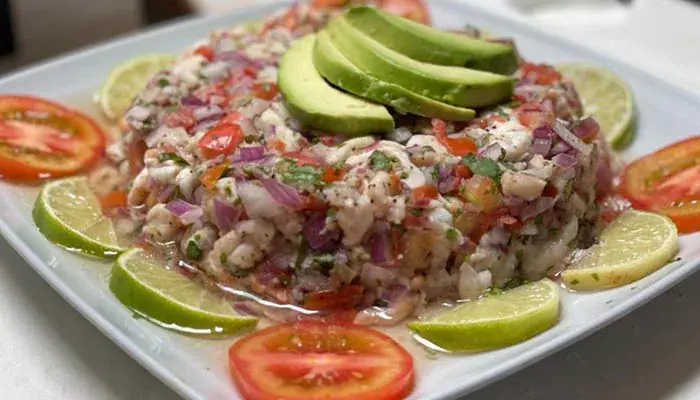 Fish ceviche with red onion and cilantro, crowned with avocado slices and ringed by lime and tomato
