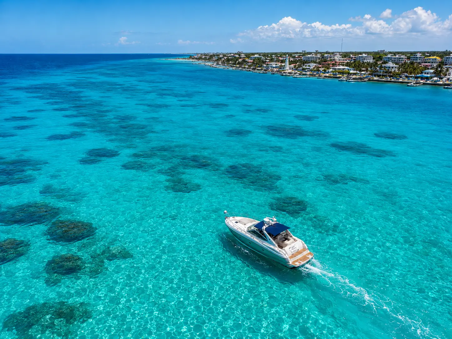 Aerial view of a motor yacht gliding over turquoise reef shallows off the Cancún coastline