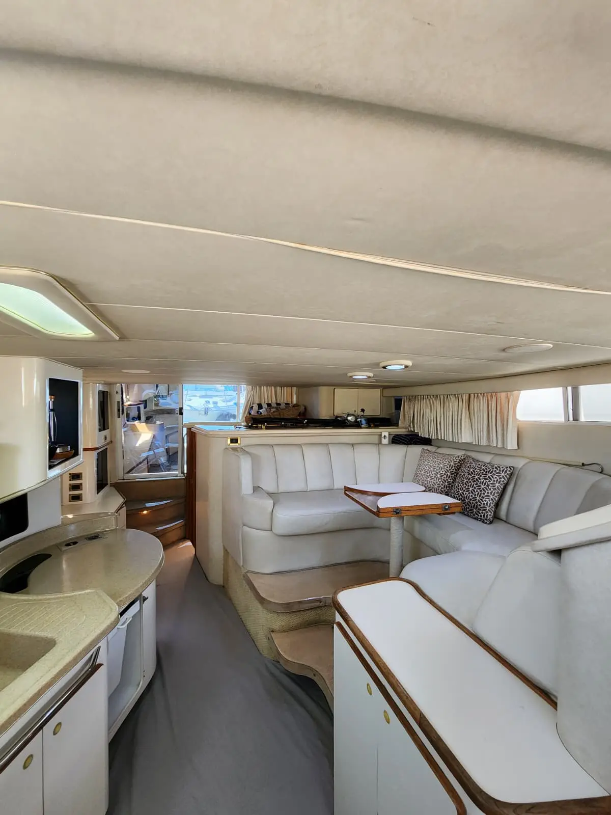 Bright yacht salon with white leather seating, a dinette table and galley counter