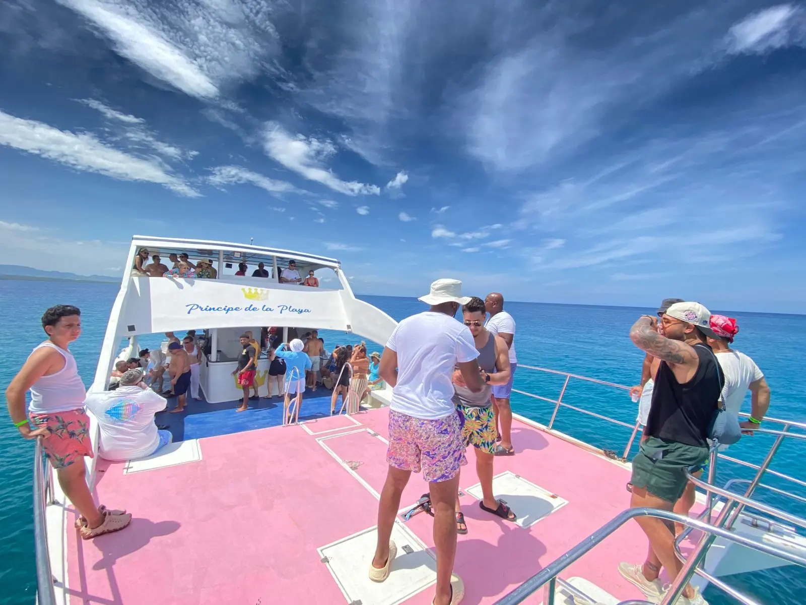 Guests mingling on the pink foredeck of a two-deck power catamaran off Puerto Plata