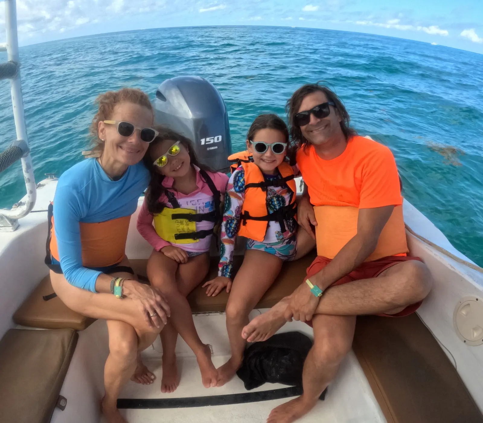 Family with two girls in life vests smiling on the speedboat's stern seat on open blue water