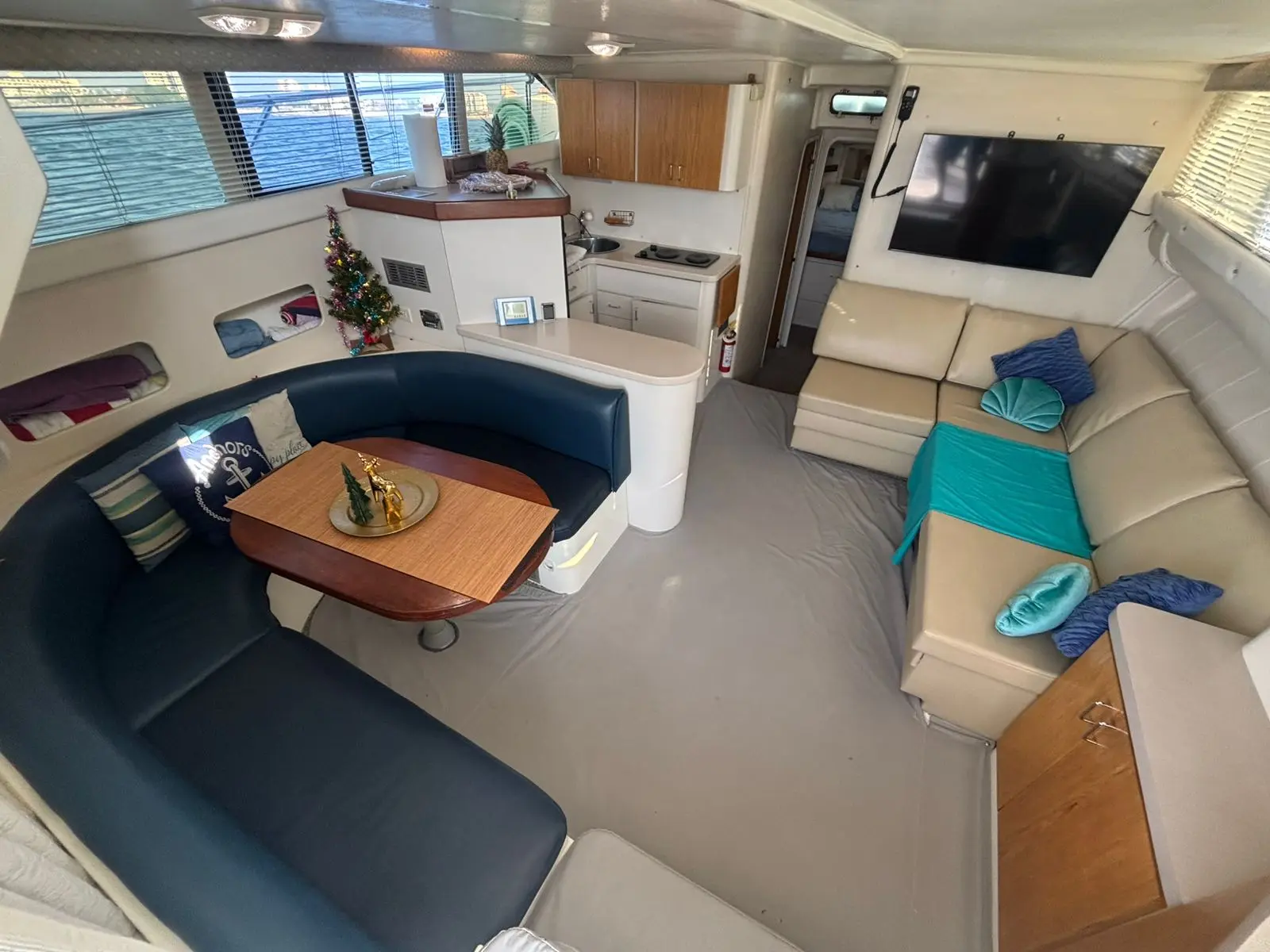 Yacht salon with a navy U-shaped dinette, cream sofa with teal cushions and a galley behind