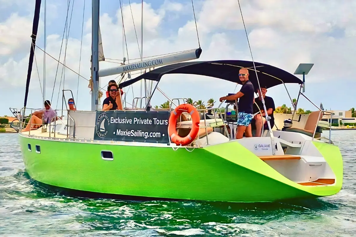 Lime-green sailing yacht with guests on deck cruising across turquoise water in Curaçao