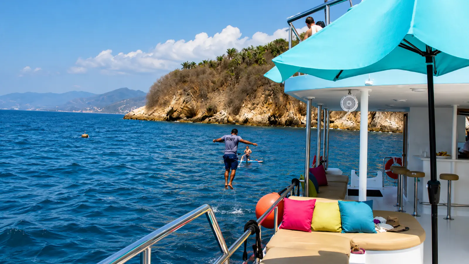 Guest jumping from the catamaran's deck into deep blue water by a green rocky islet off Puerto Vallarta