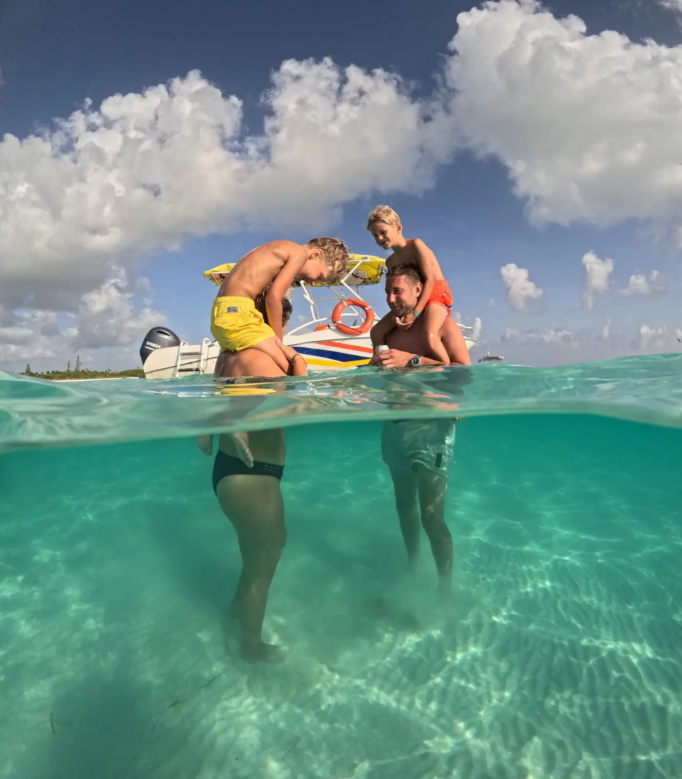 Over-under shot of friends horsing around in shallow turquoise water near a speedboat in Cozumel