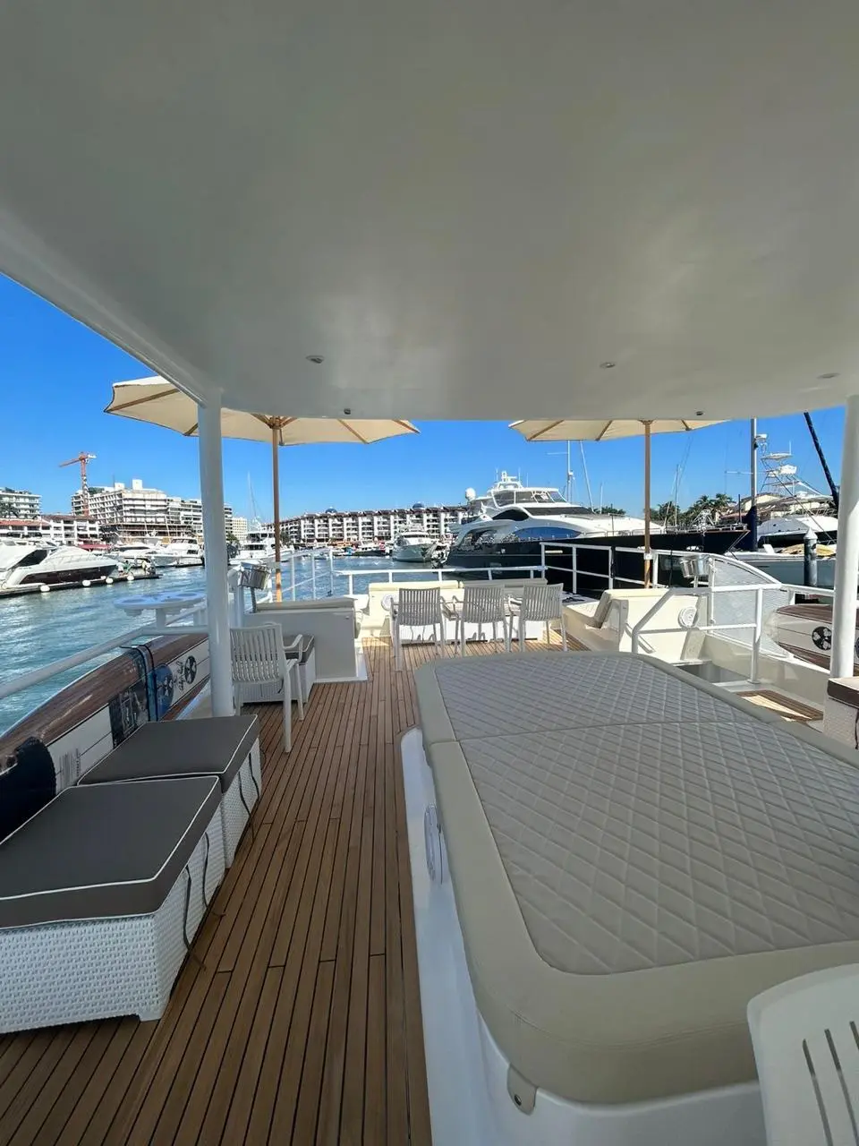 Shaded teak deck of the catamaran with cushioned benches and a large padded lounger at the marina