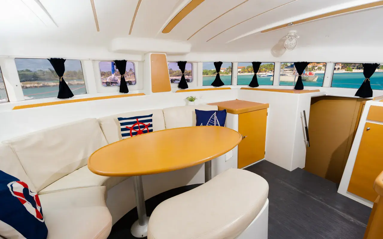 Catamaran saloon with a curved cream settee, oval wooden table and panoramic windows