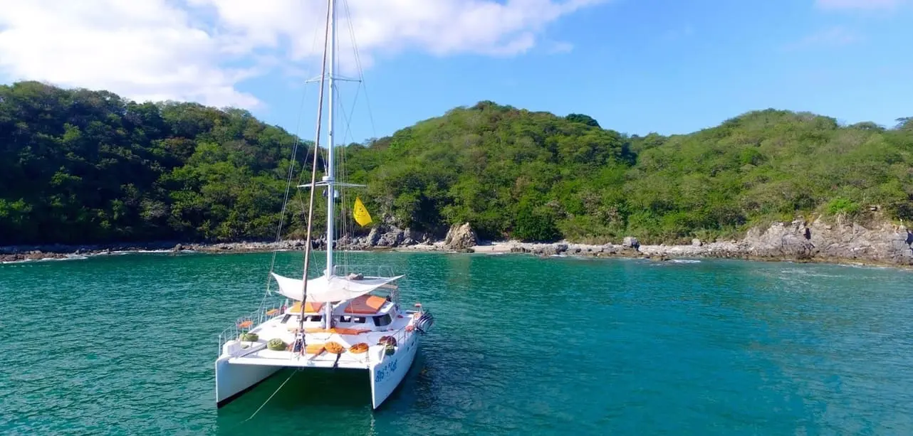 Sailing catamaran anchored in a turquoise cove beneath jungle-covered hills near Puerto Vallarta
