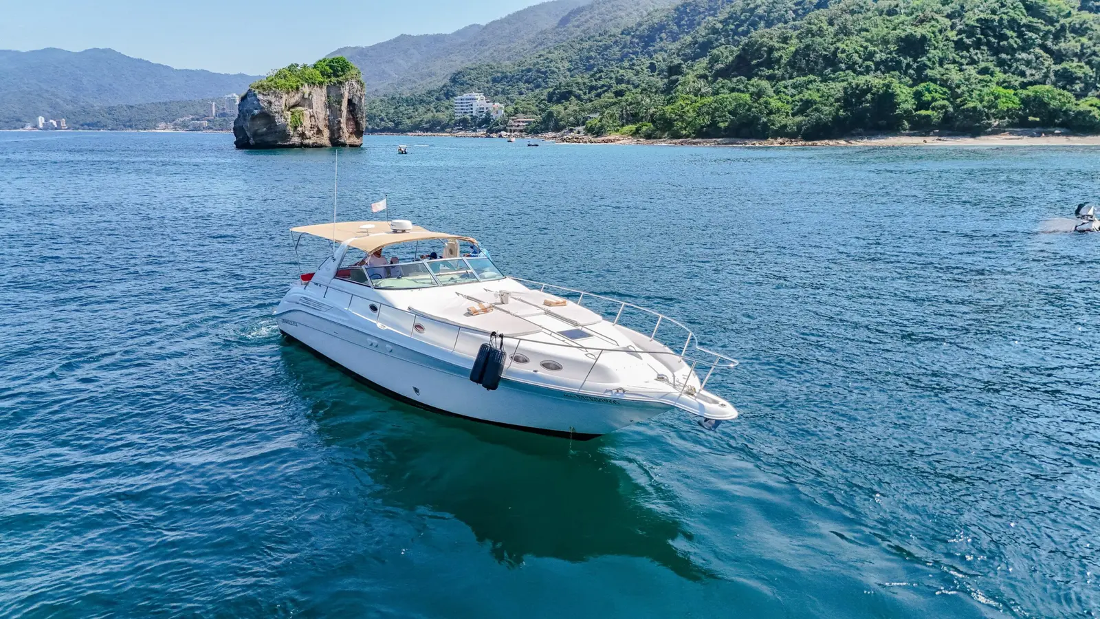 A white motor yacht at anchor in calm blue water below the jungle hills of Puerto Vallarta