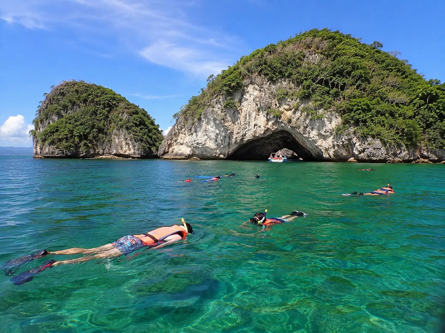 Snorkelers float in clear green water in front of a rock arch at Los Arcos Marine Park