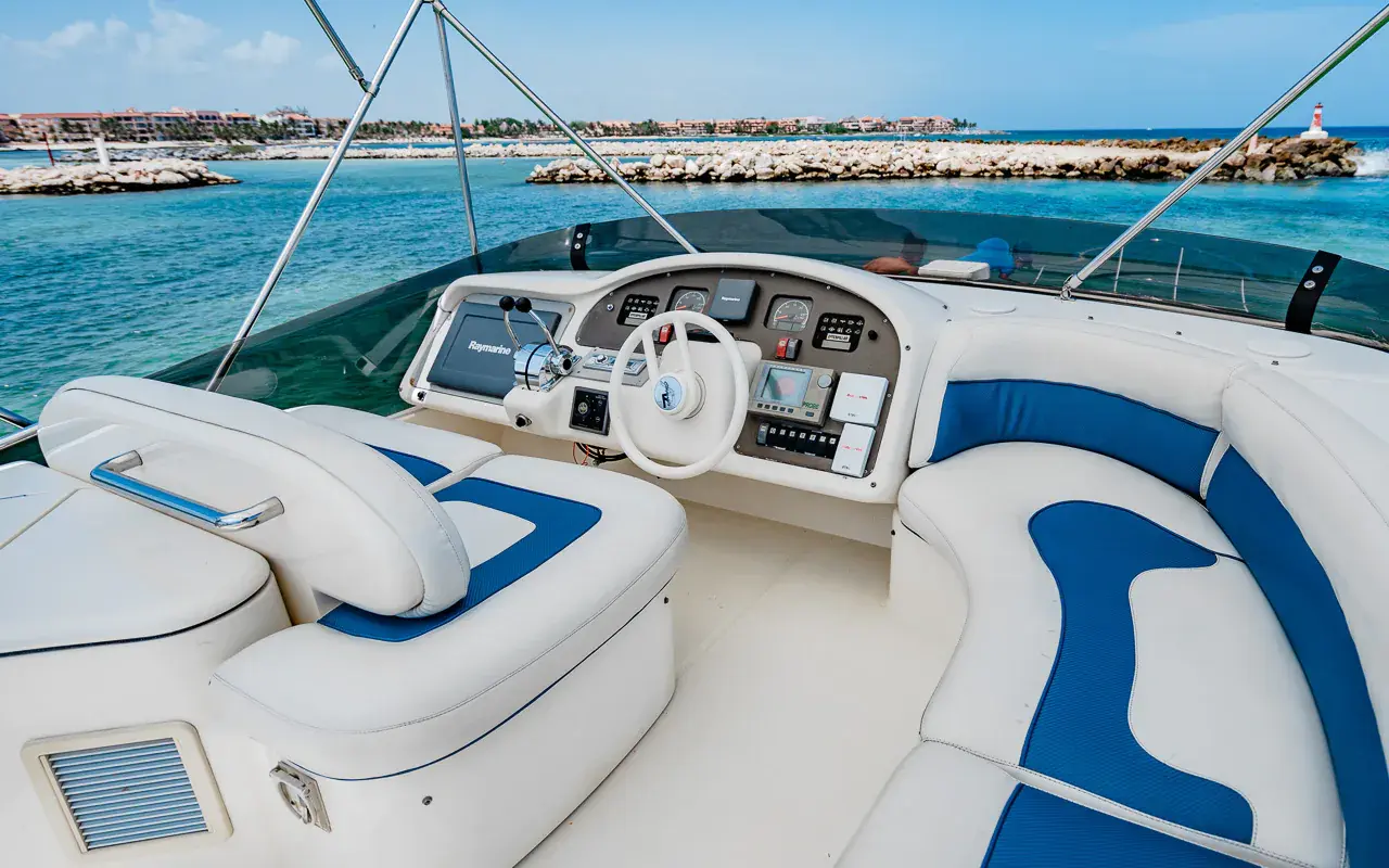 Yacht's flybridge helm with a steering wheel and blue-and-white seats, a Riviera Maya marina beyond