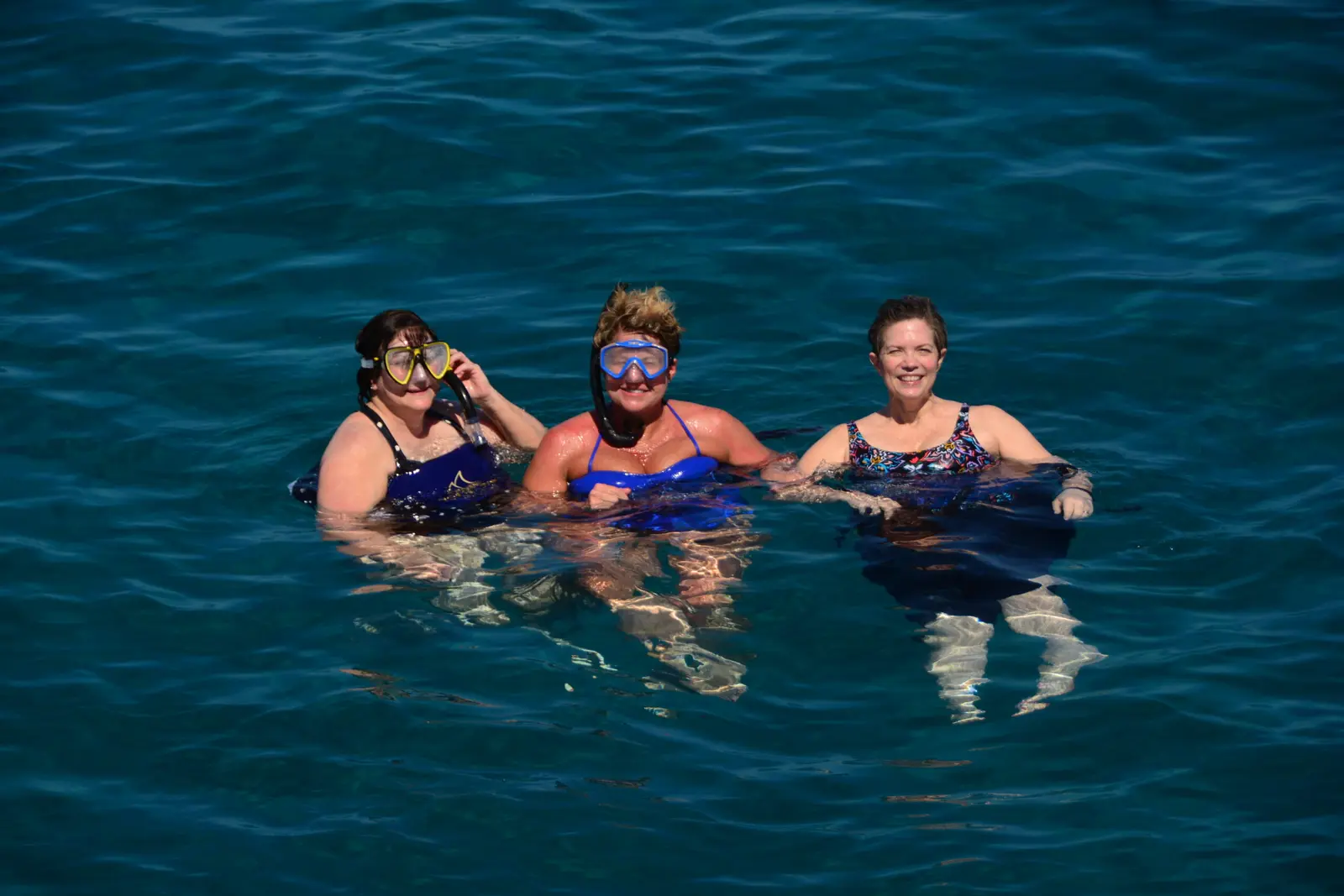 Three women with snorkel masks smiling together in deep blue water