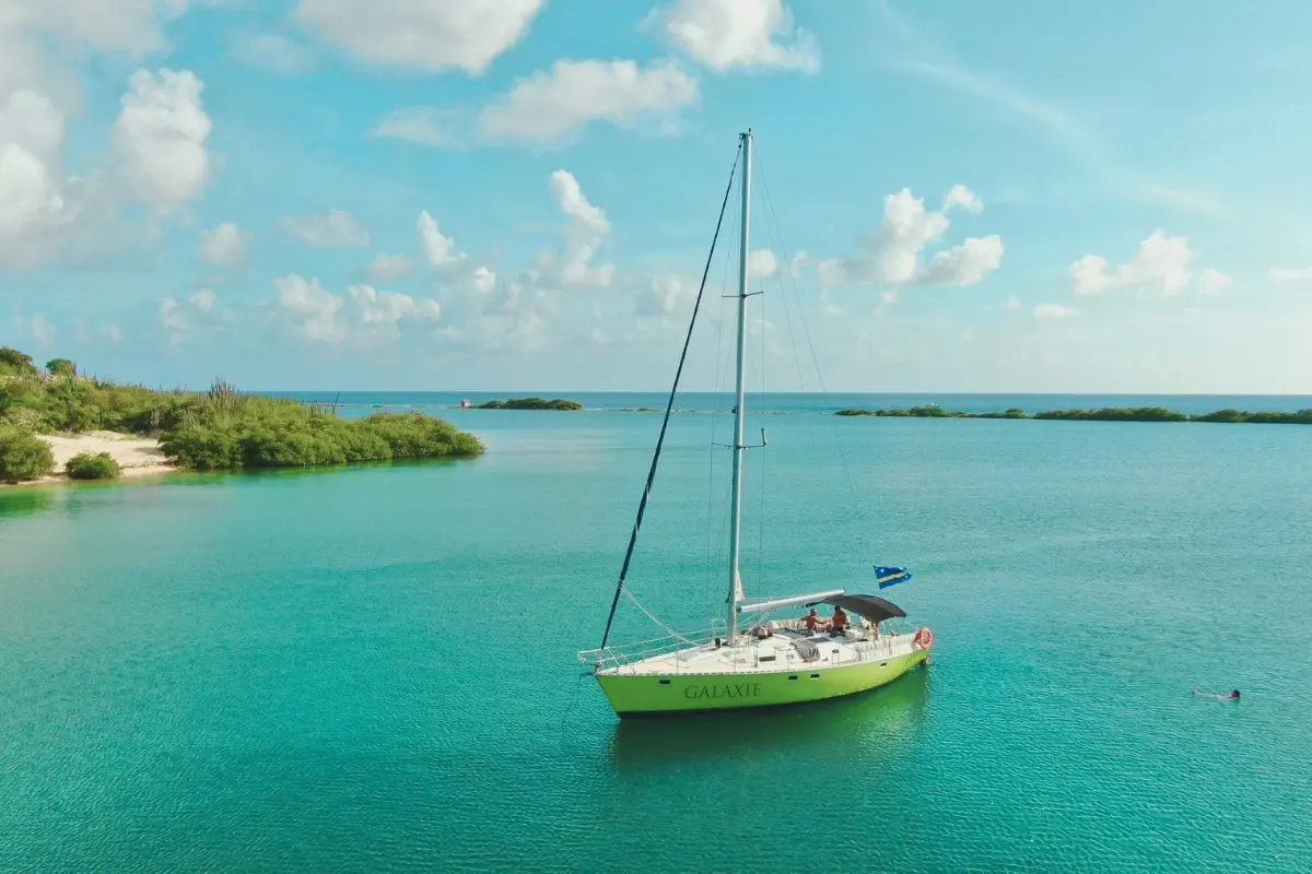 Aerial view of a lime-green sailing yacht at anchor in a quiet turquoise Curaçao bay