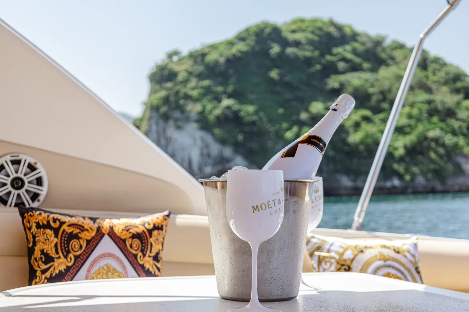 A bottle chilling in an ice bucket beside a white flute and patterned cushions on the yacht