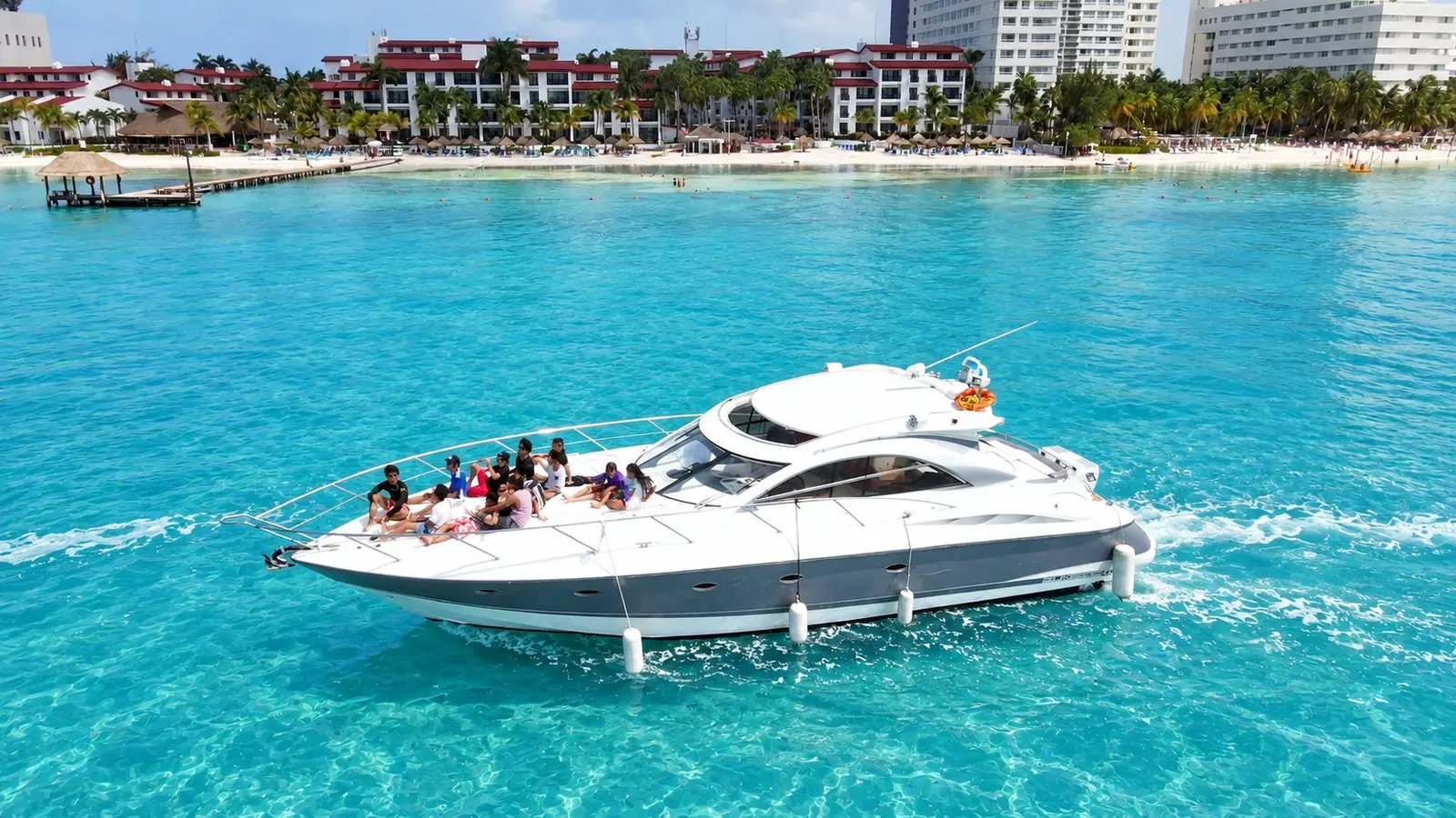 Sport yacht with guests on the bow cruising turquoise water past beachfront hotels in Cancún