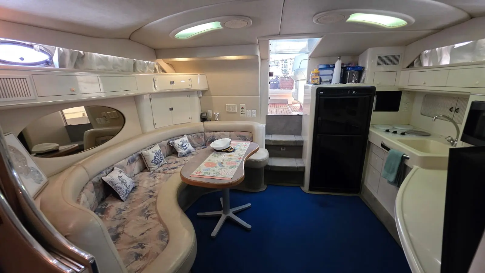 Wide view of the yacht cabin with a curved dinette, galley fridge and sink, and steps up to the deck