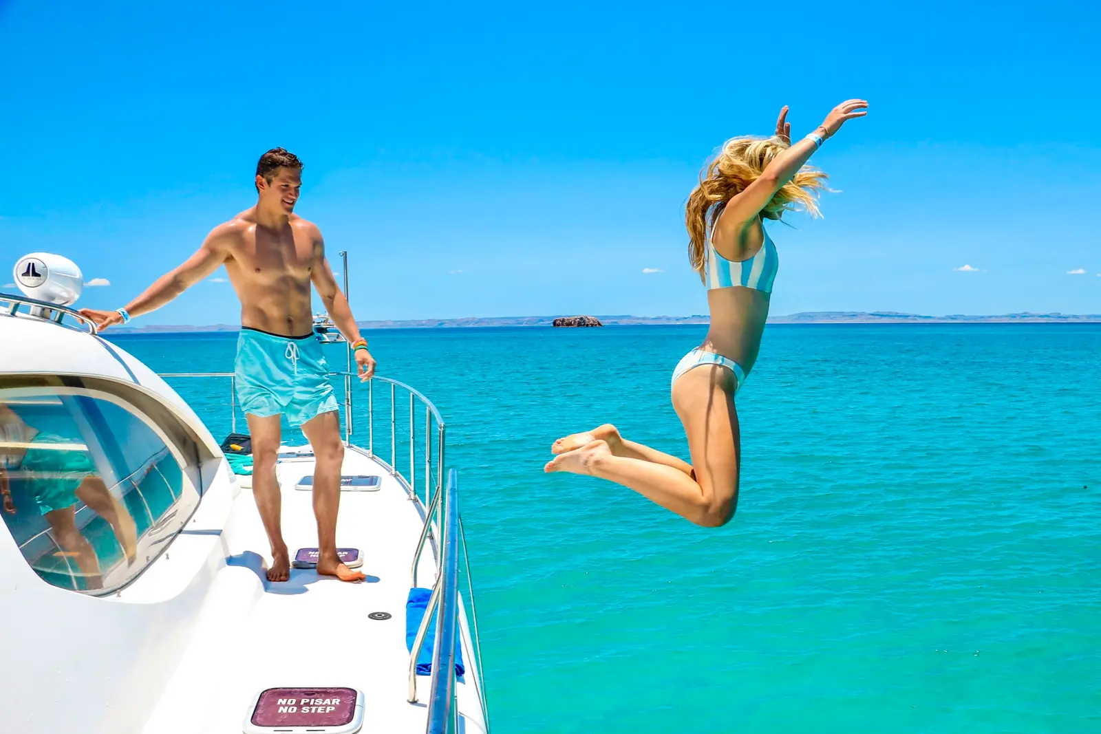 A woman leaps from the yacht's side deck into turquoise water as a man looks on