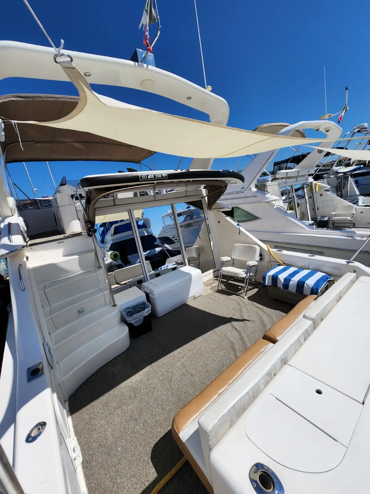 Carpeted aft cockpit of the yacht with a striped cushion and cooler under a canvas sunshade