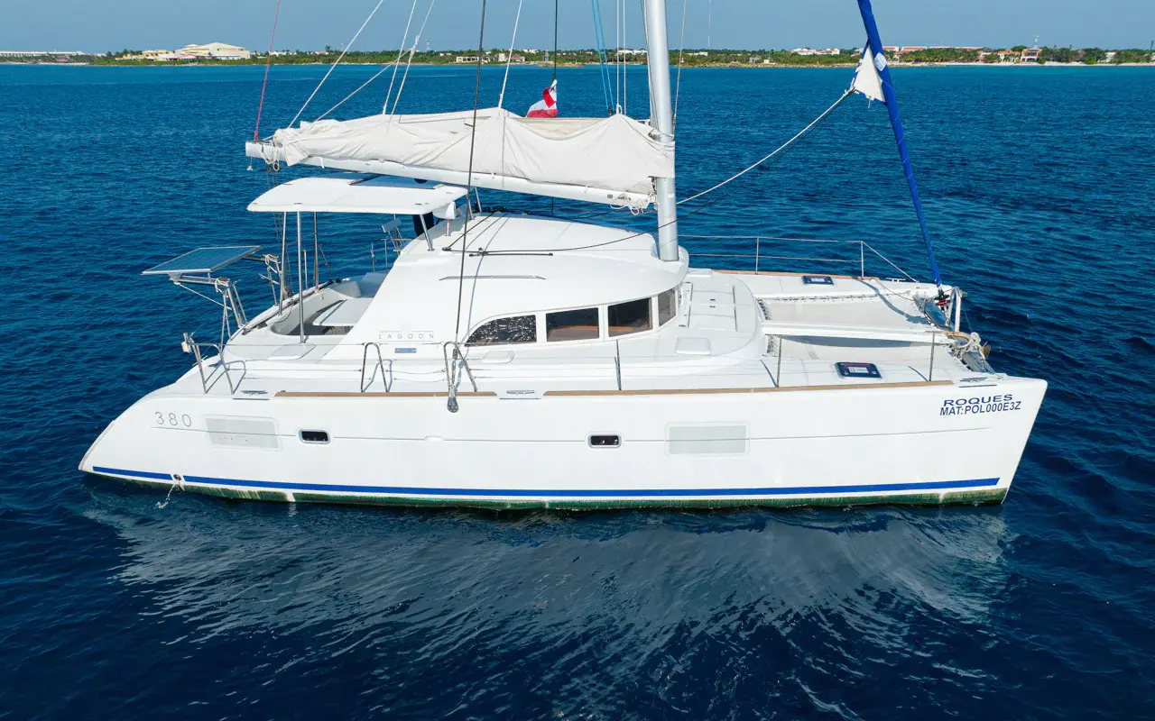 Sailing catamaran at anchor with its mainsail furled on the boom, Riviera Maya coast behind