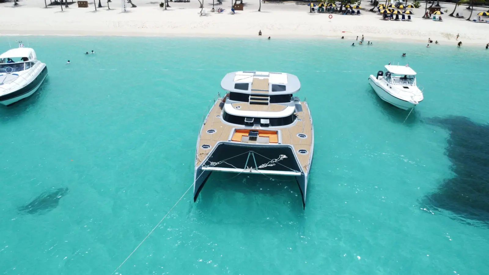 Aerial view of a catamaran anchored off a white-sand beach near Punta Cana, two motorboats nearby