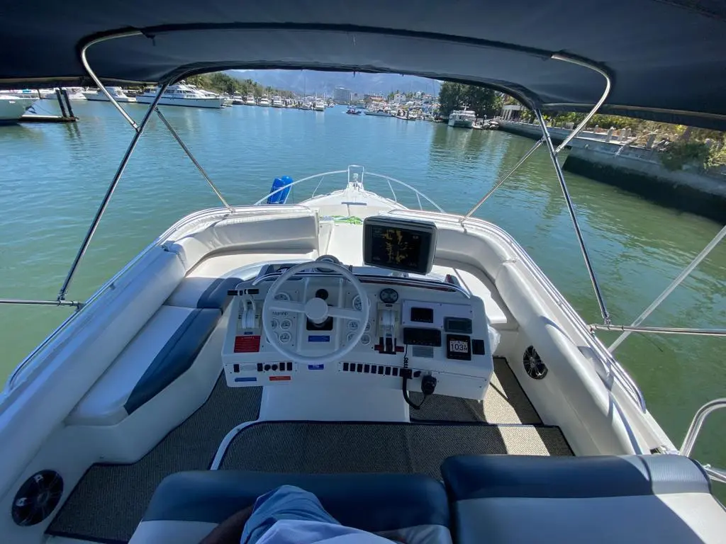 Flybridge helm with steering wheel and navigation screen, looking over the yacht's bow down a marina channel