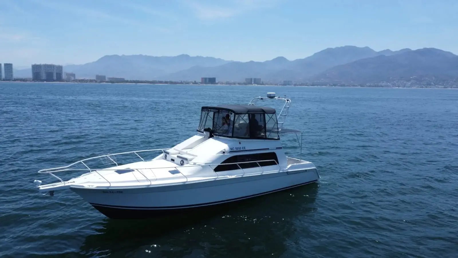 A white flybridge yacht floats on calm water with hazy mountains and the city skyline beyond