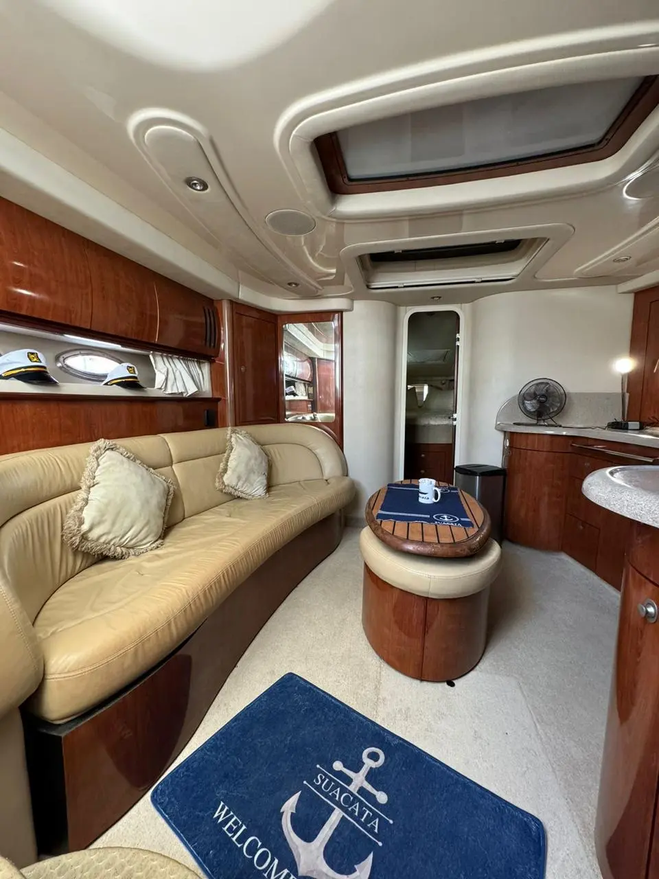 Yacht salon with a cream leather sofa, cherry wood cabinets and an anchor welcome mat