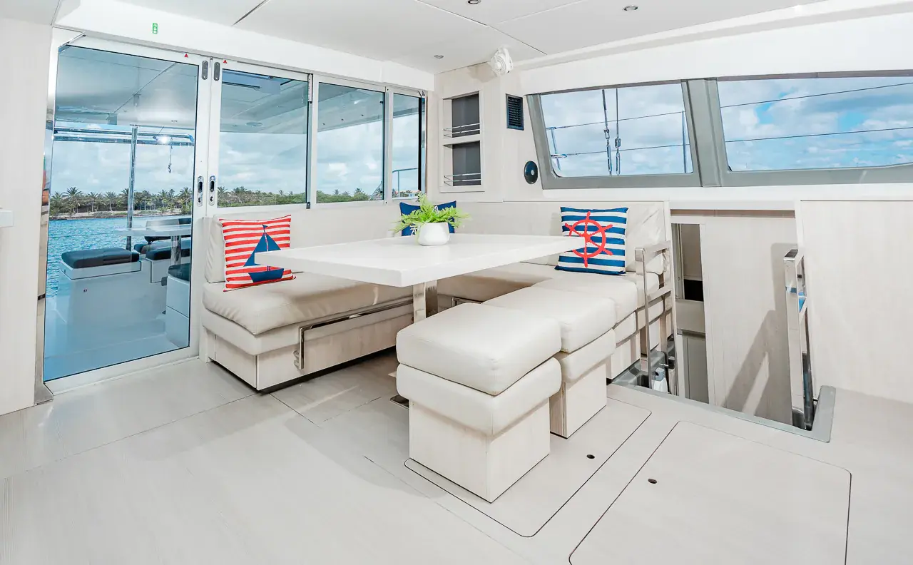 Bright catamaran saloon with a white dinette, striped nautical cushions and wide windows