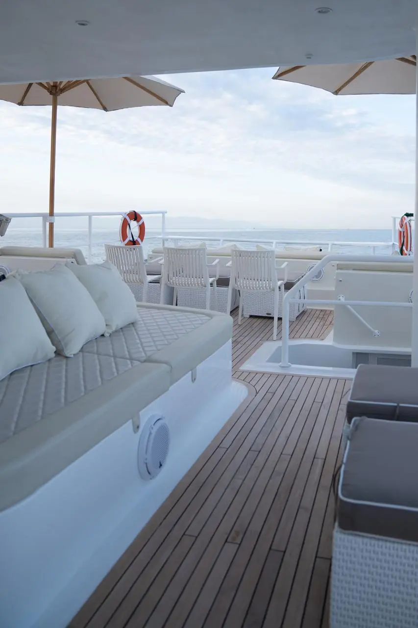 Teak upper deck of the catamaran lined with cushioned benches, white chairs and parasols at the far end
