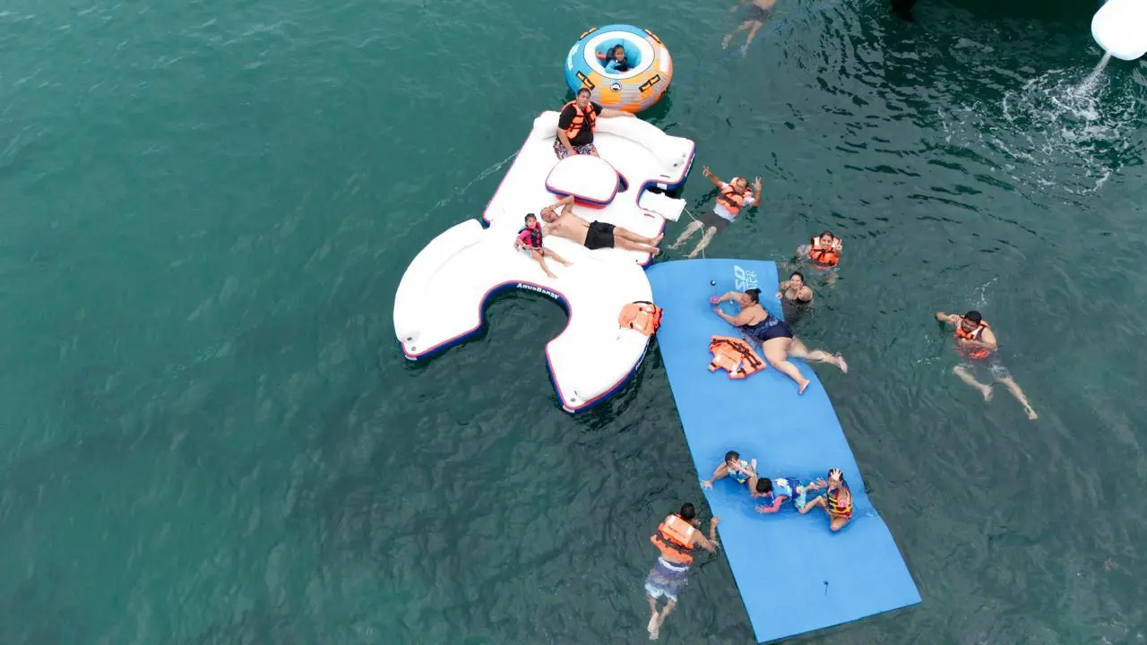 Overhead view of guests in life jackets swimming around an inflatable platform and a blue floating mat