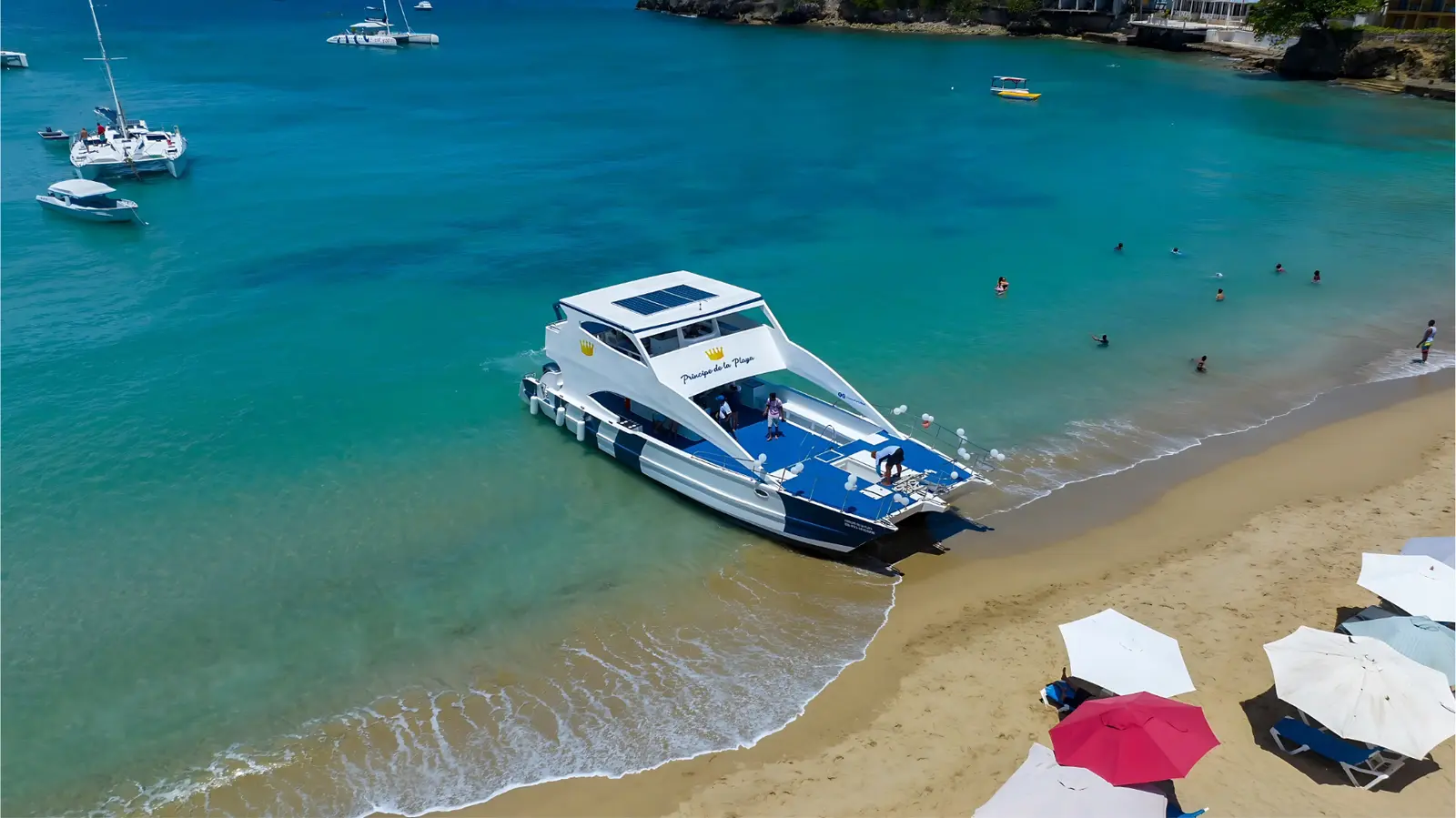 Power catamaran moored at a golden sand beach near Puerto Plata, with umbrellas ashore and swimmers in the bay