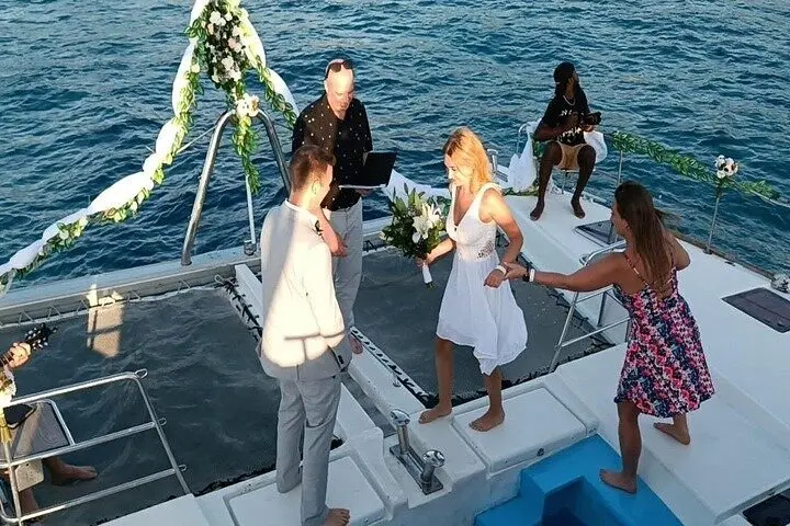 Wedding ceremony on a flower-decked catamaran bow off Puerto Plata, a couple in white before an officiant