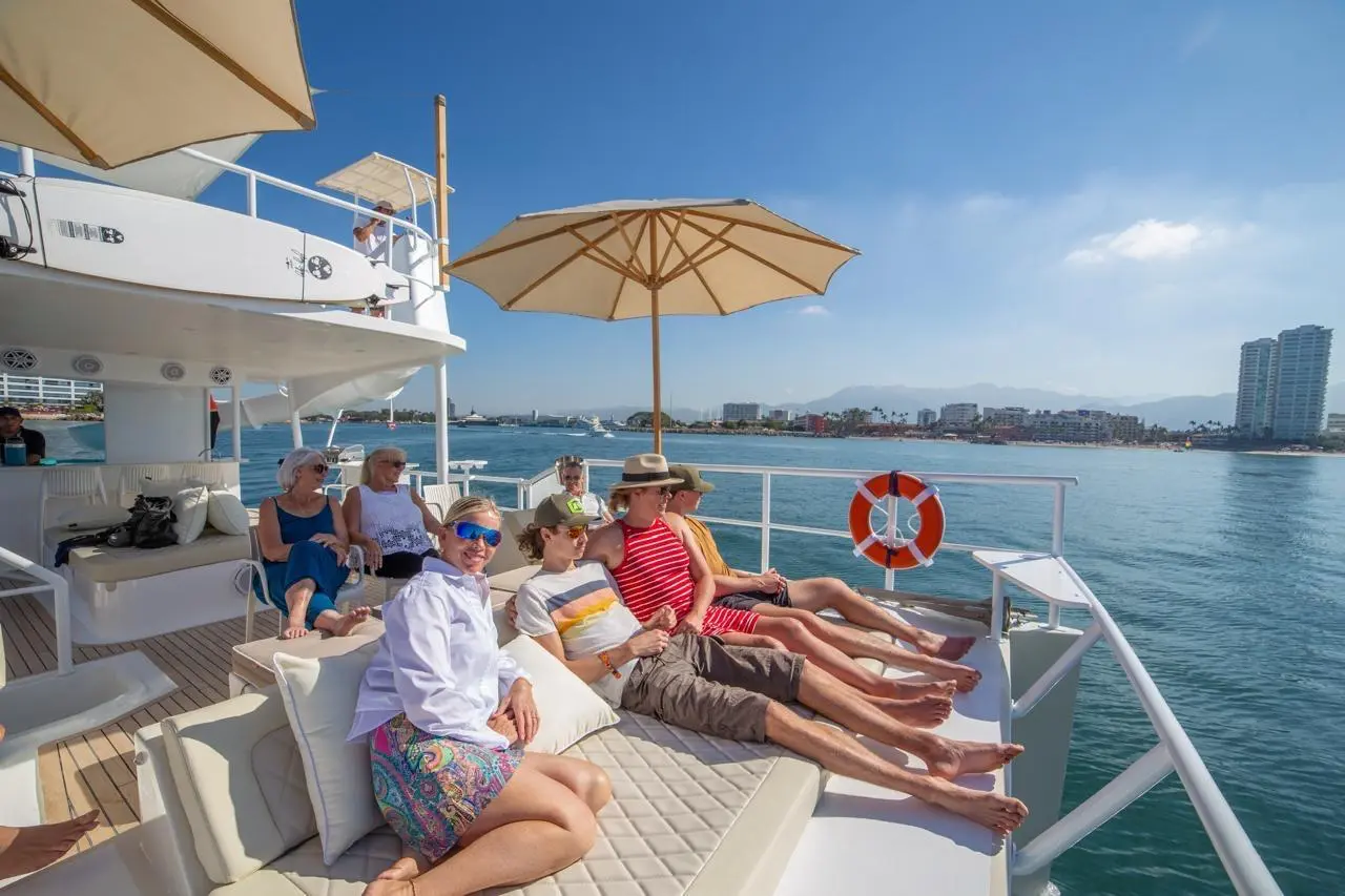 Guests stretch out on sun pads under parasols at the front of the catamaran, Puerto Vallarta high-rises behind
