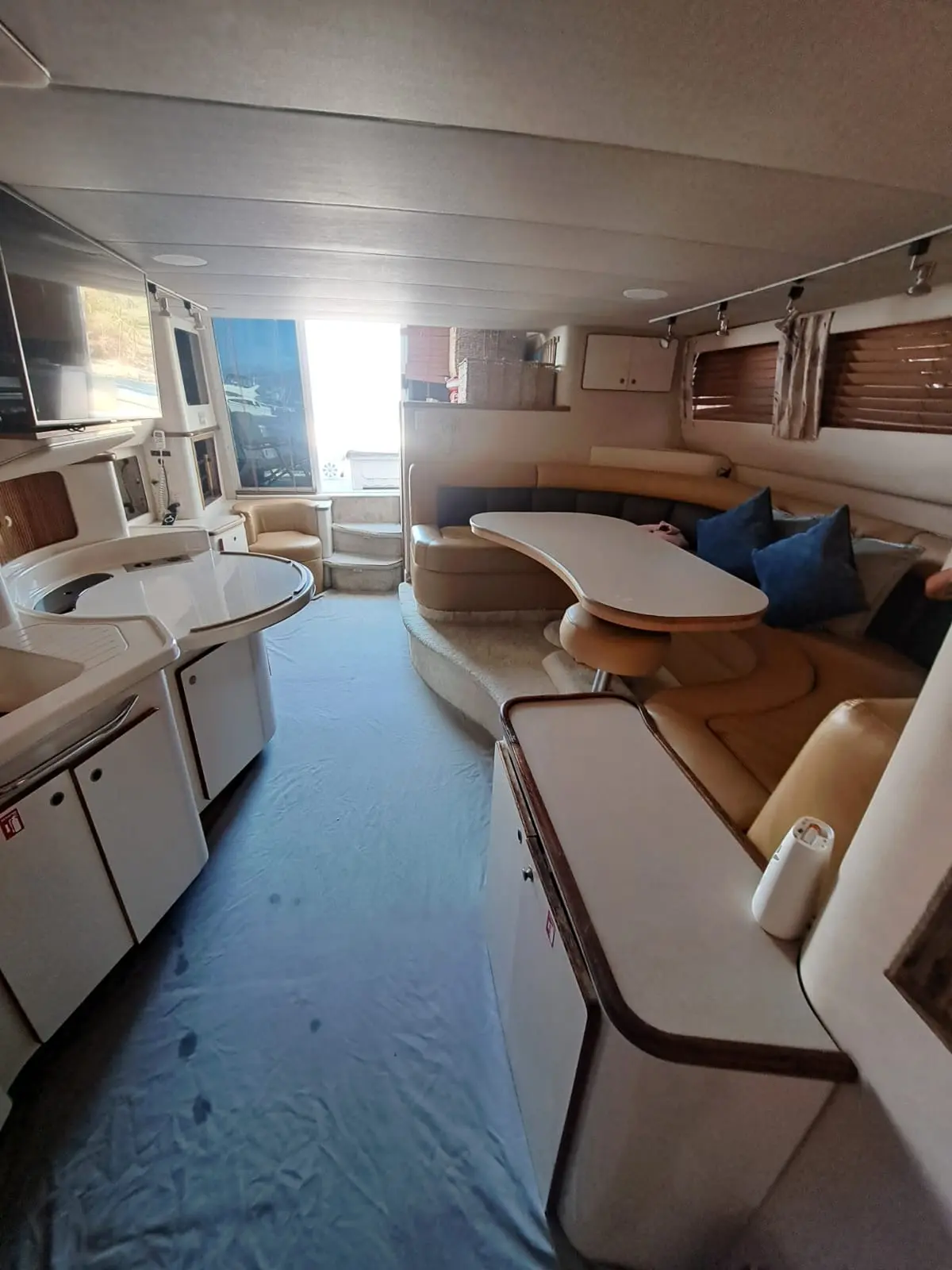 The yacht's interior salon with a galley, cream sofa seating with blue pillows and a dining table