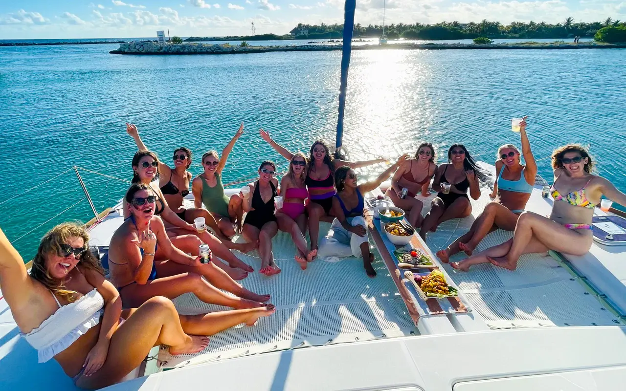 Group of women cheering around a snack platter on the catamaran's foredeck