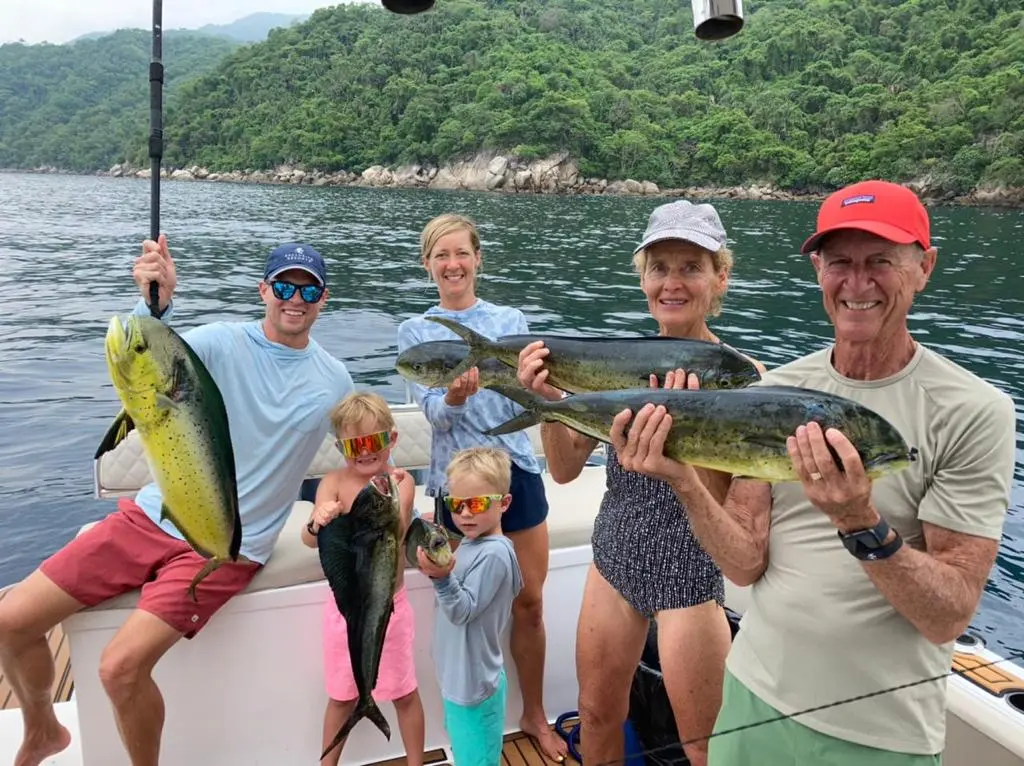 Family with two kids showing off their mahi-mahi catch on the boat below the jungle hills of Puerto Vallarta