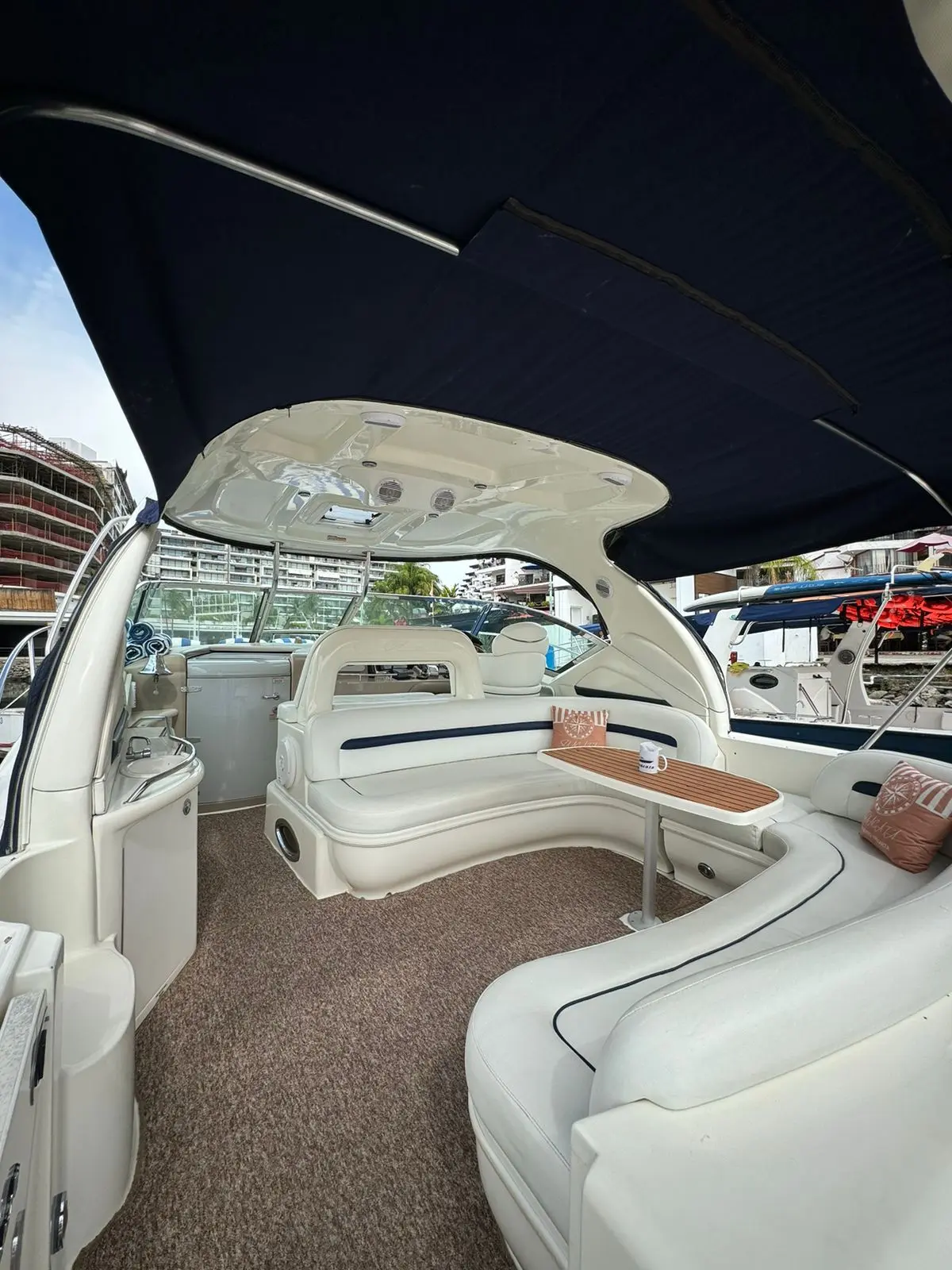 Cockpit of the yacht with curved white seating and a table under a navy canvas sunshade