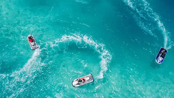 Three jet skis create ripples in bright blue water.
