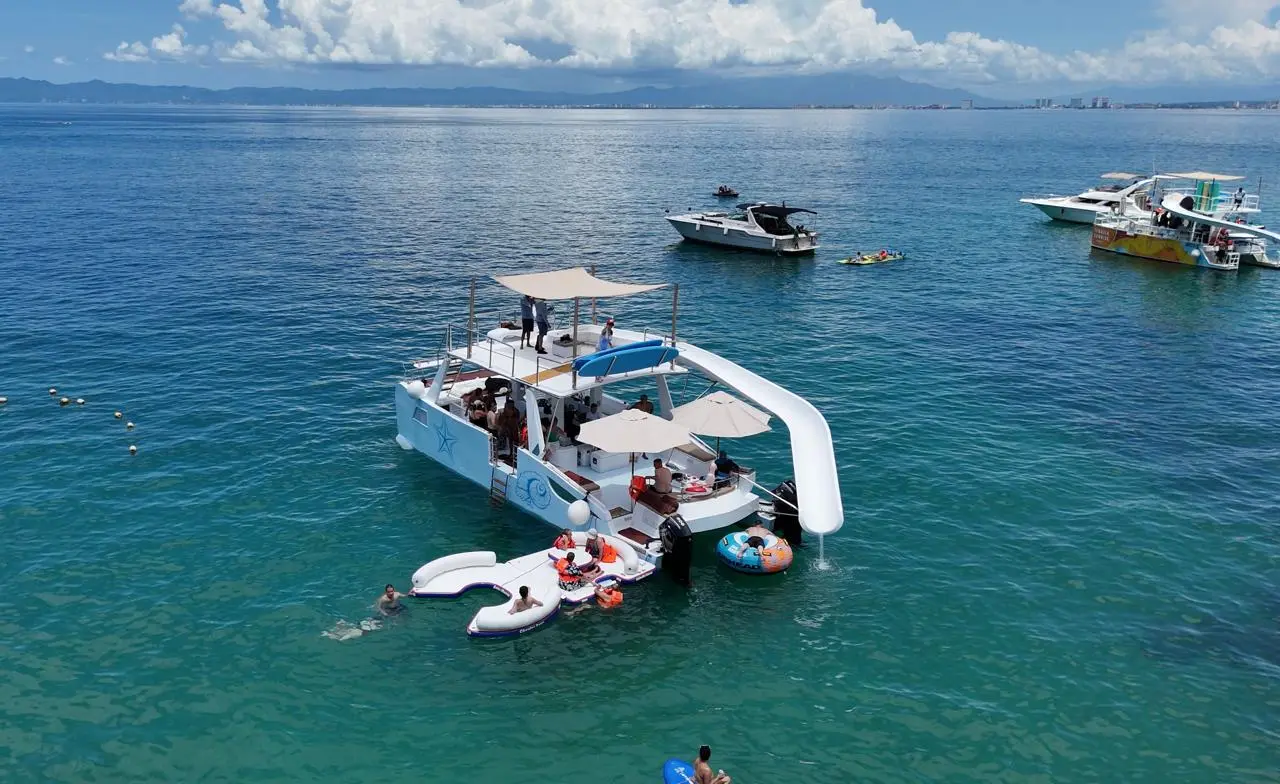 Guests swimming with inflatable floats beside the party catamaran, yachts anchored nearby off Puerto Vallarta