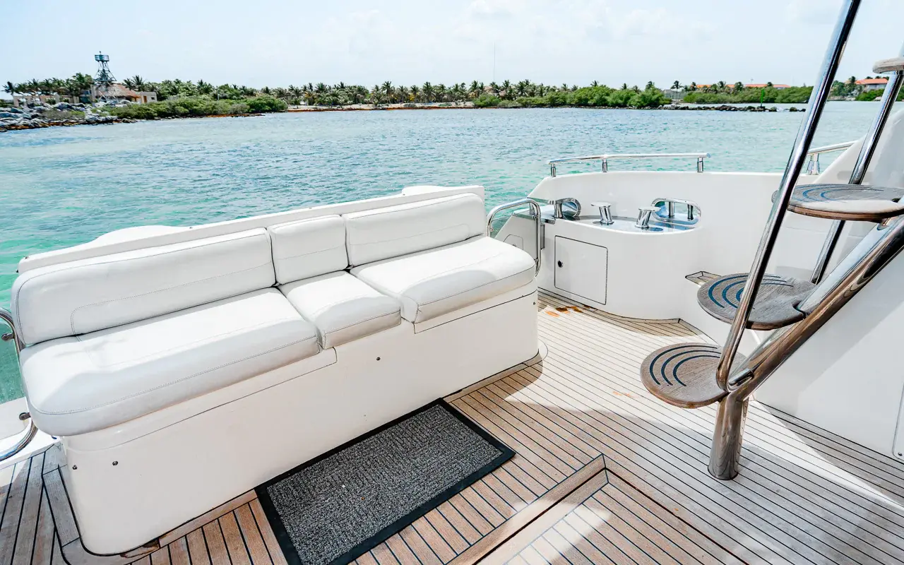 Teak aft deck of the yacht with a white bench seat and flybridge ladder, green Riviera Maya shore behind