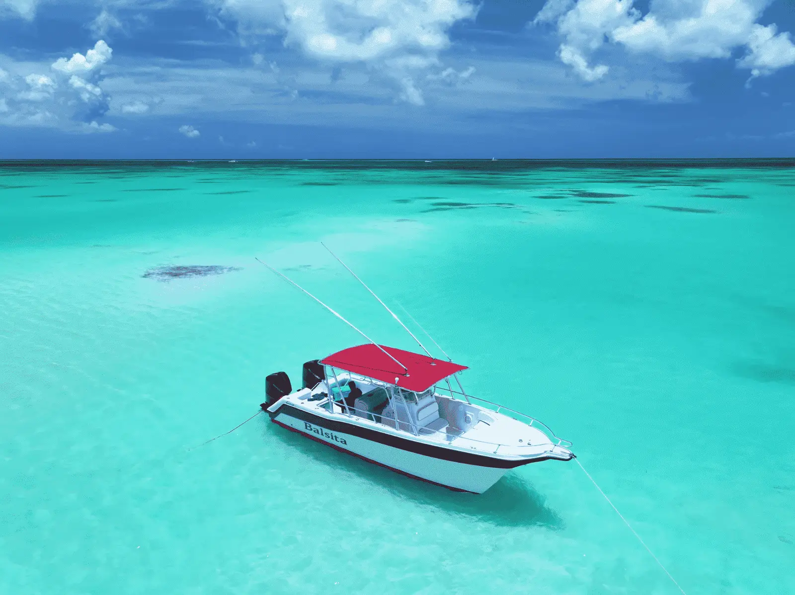 Speedboat with a red canopy anchored in shallow turquoise water near Saona Island