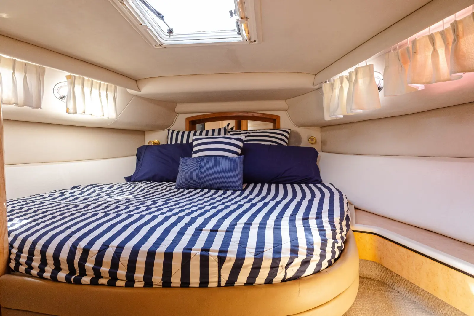 Yacht cabin with a navy and white striped double bed beneath an overhead skylight hatch