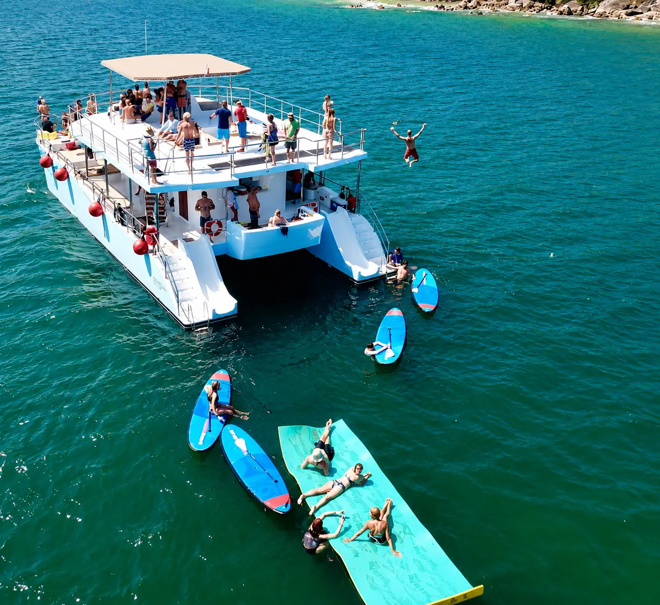Overhead view of guests on paddleboards and a floating water mat beside the catamaran off Puerto Vallarta